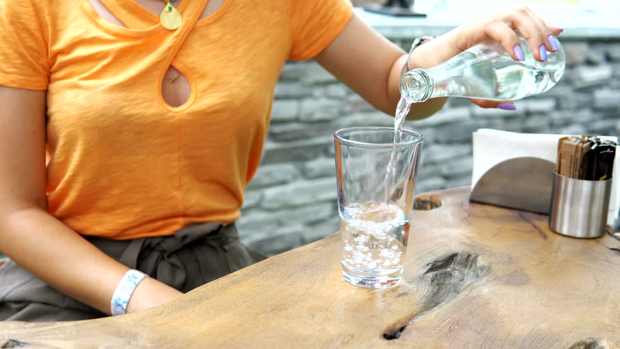 mujer vertiendo agua fría en un vaso. joven chica morena abre y vierte agua fría embotellada en el vaso