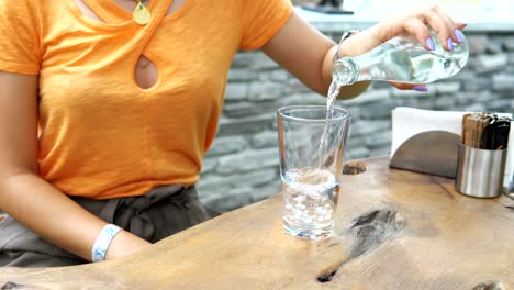 woman pouring chilled water in glass. young brunette girl opens and pours cold bottled water in glass