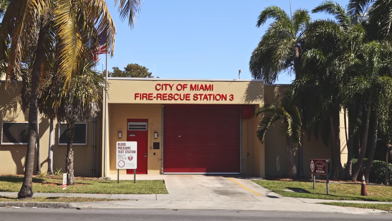 A wide view of Miami Fire Station 3’s garage shows its place in the city, surrounded by tropical greenery and a proudly waving American flag.
