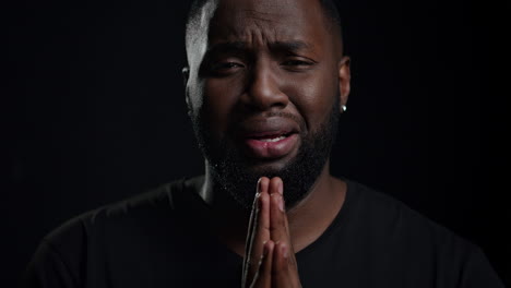 Depression-afro-guy-looking-at-camera-on-black-background.-Man-crying-indoors