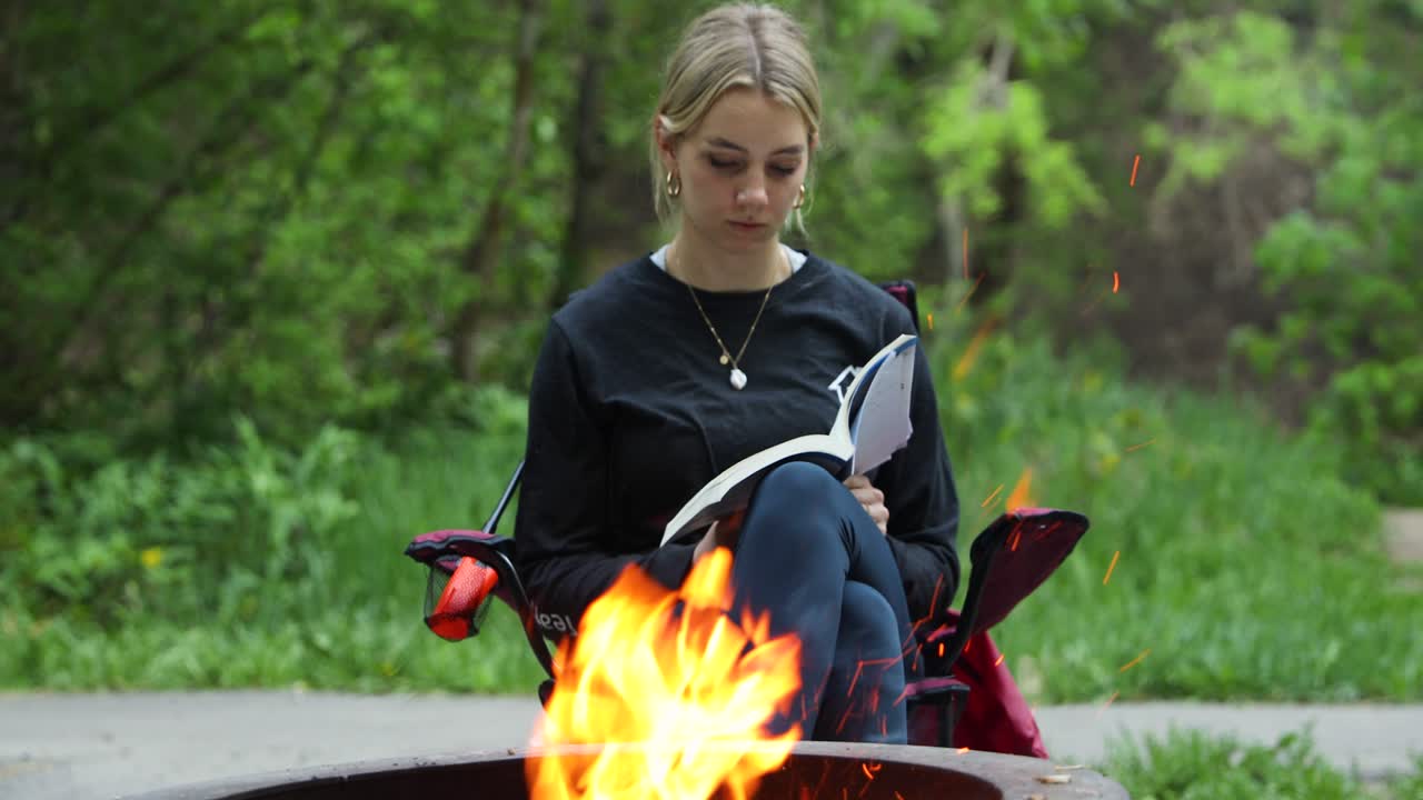 mujer joven leyendo pacíficamente un libro junto a la fogata, relajándose al aire libre de vacaciones