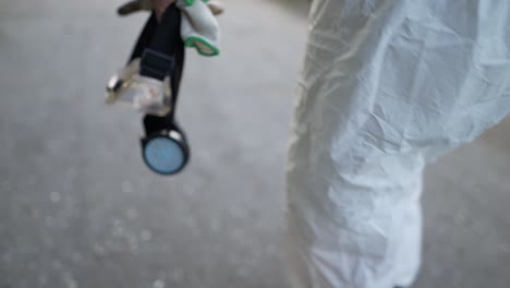 unrecognizable worker in protective suit walks with mask and gloves in hand