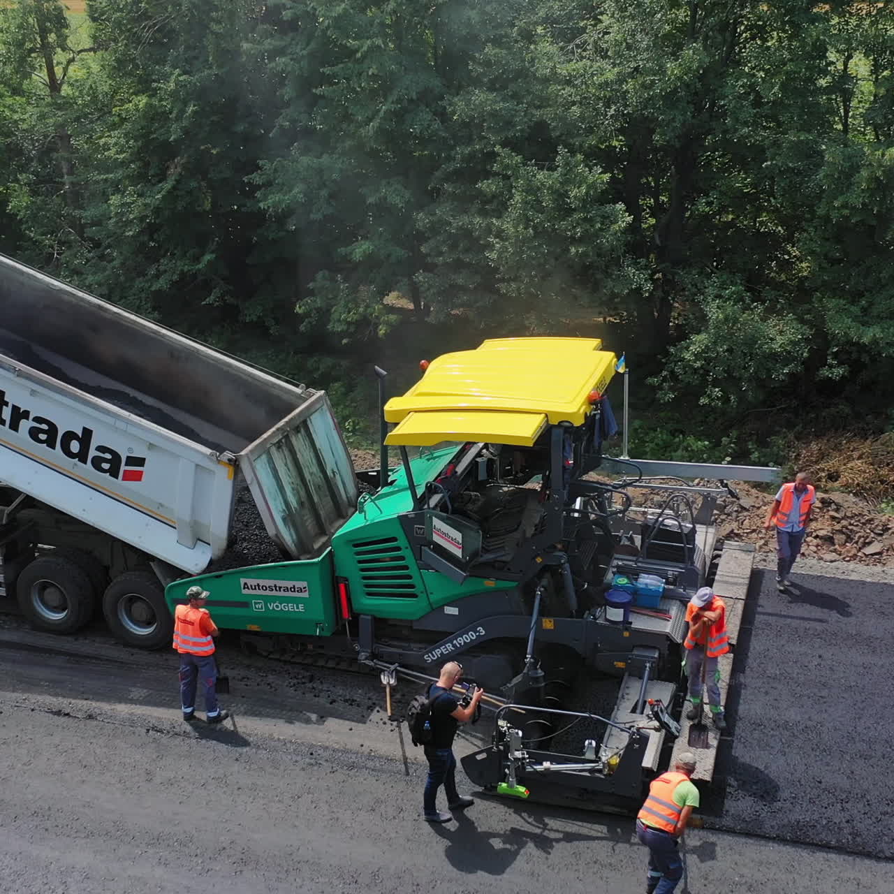 Road works on asphalt pavement construction. Heavy machinery on the road. Workers in orange uniform leveling up hot asphalt on the highway. Aerial view.
