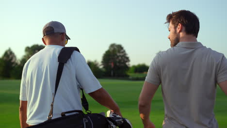 Dad-son-going-fairway-course.-Two-golfers-take-sport-equipment-clubs-outdoors.