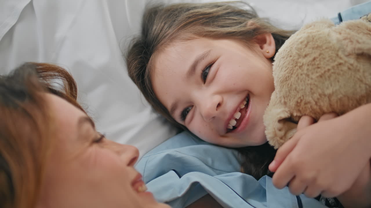 Small girl touching mother holding toy at bedroom closeup. Mom kissing daughter