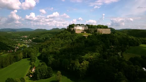 vista de drones en un castillo monumental en una colina que desciende más y más cerca del suelo y los árboles mientras se ve el monumento en sajonia alemania en un día parcialmente soleado