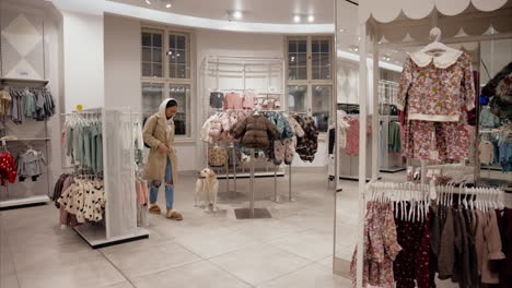 young woman is laughing at her dog while he scratches his ears in a children's clothing store