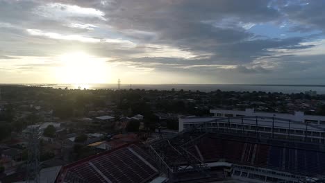 Drone-take-aerial-shot-of-the-city-of-Parintins-located-in-Amazonas,-Brazil-as-the-sun-sets-in-the-horizon