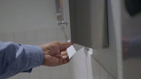 person taking a paper towel from a dispenser in a bathroom