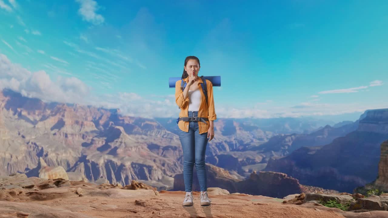 Full Body Of Asian Female Hiker With Mountaineering Backpack Looking At Camera And Making Shh Gesture While Traveling At The Top Of Mountain