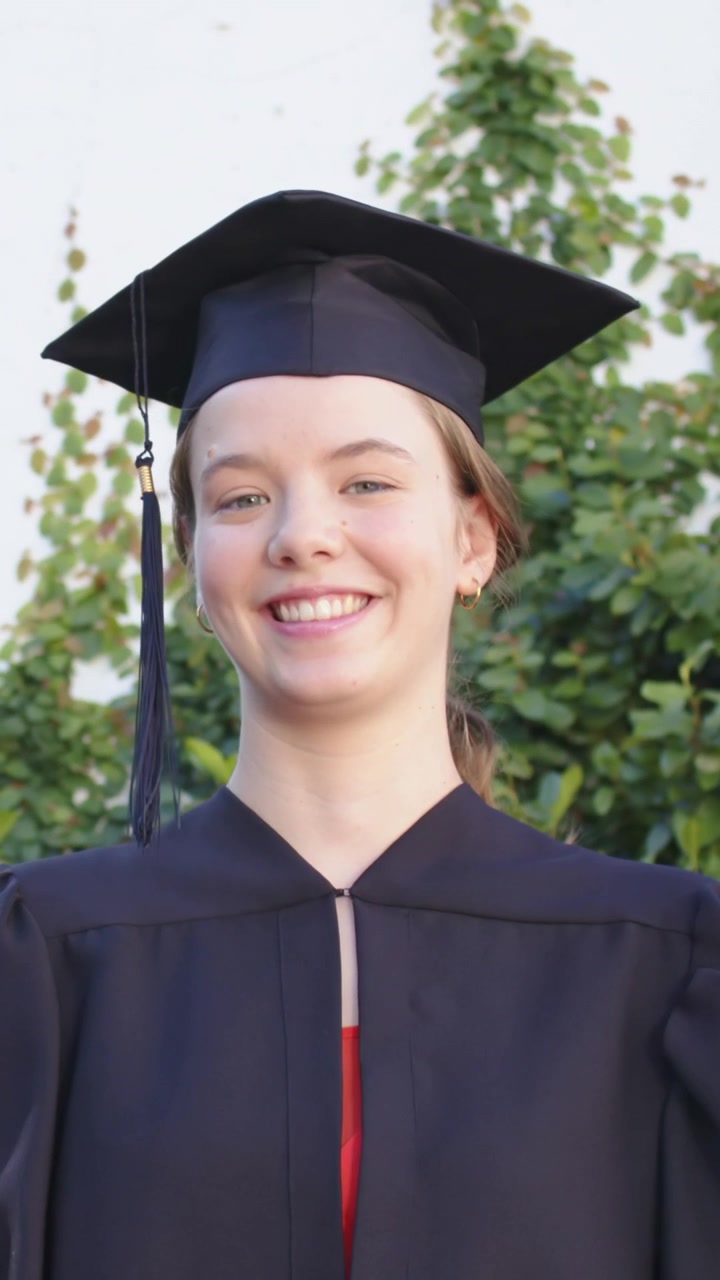 Video verticale: Guardando il diploma, un laureato alza la testa, sorridendo con orgoglio vicino a un muro, in toga e tocco