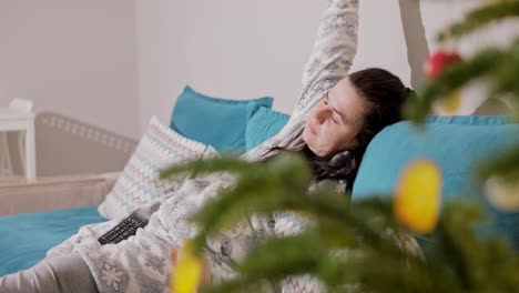 a girl sitting on the couch next to the christmas tree, watching tv - close up