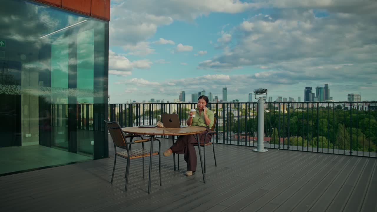 Mujer trabajando en un portátil en una terraza con vistas al paisaje urbano