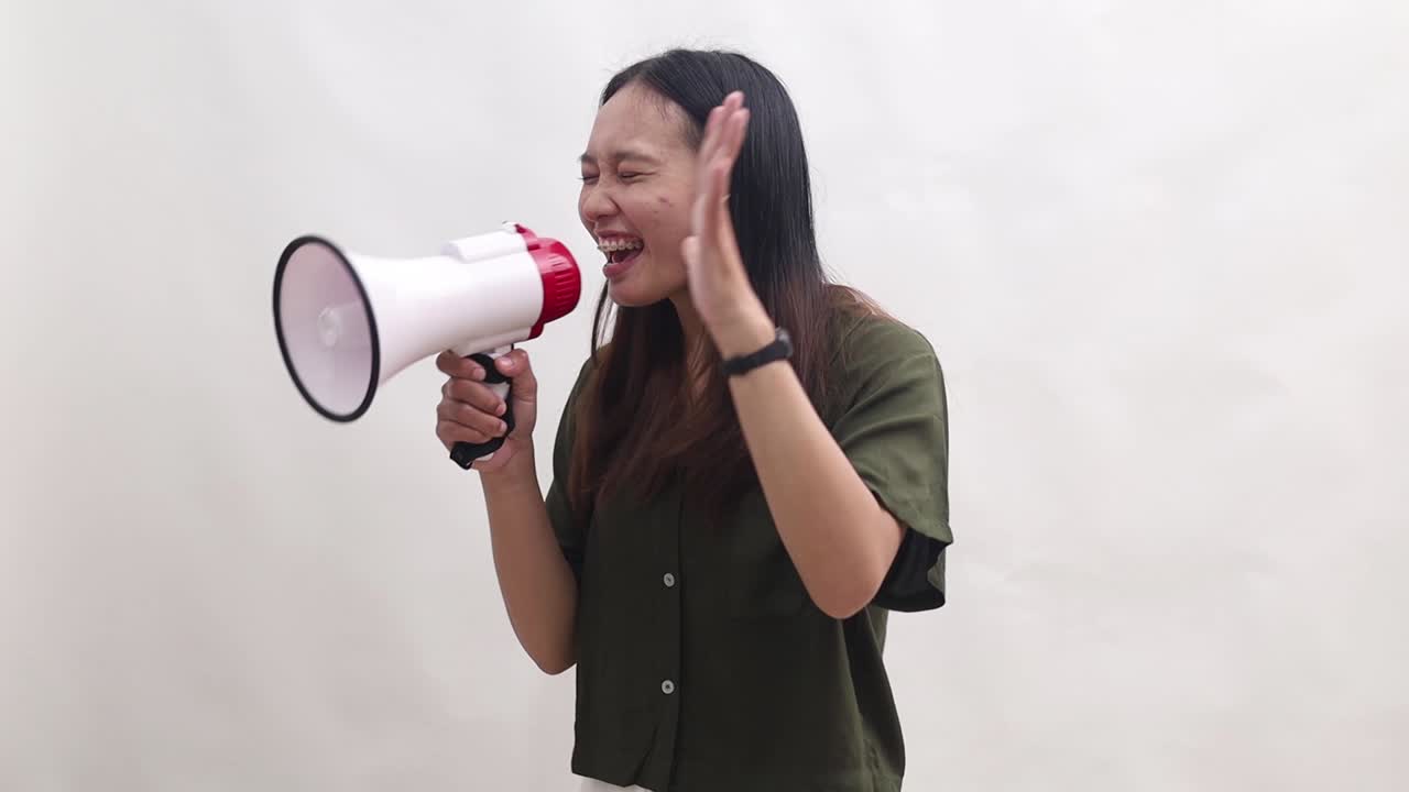 Young Asian woman wears green t-shirt scream in megaphone announces sale Hurry up to sideways isolated on white background studio portrait