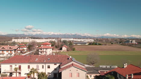 Vista-De-Vuelo-Cuesta-Arriba-Sobre-Las-Casas-Y-Campos-De-Los-Granjeros-Con-Hermosas-Montañas-En-El-Fondo-De-Arcore,-Norte-De-Italia---Toma-Aérea-De-Drones