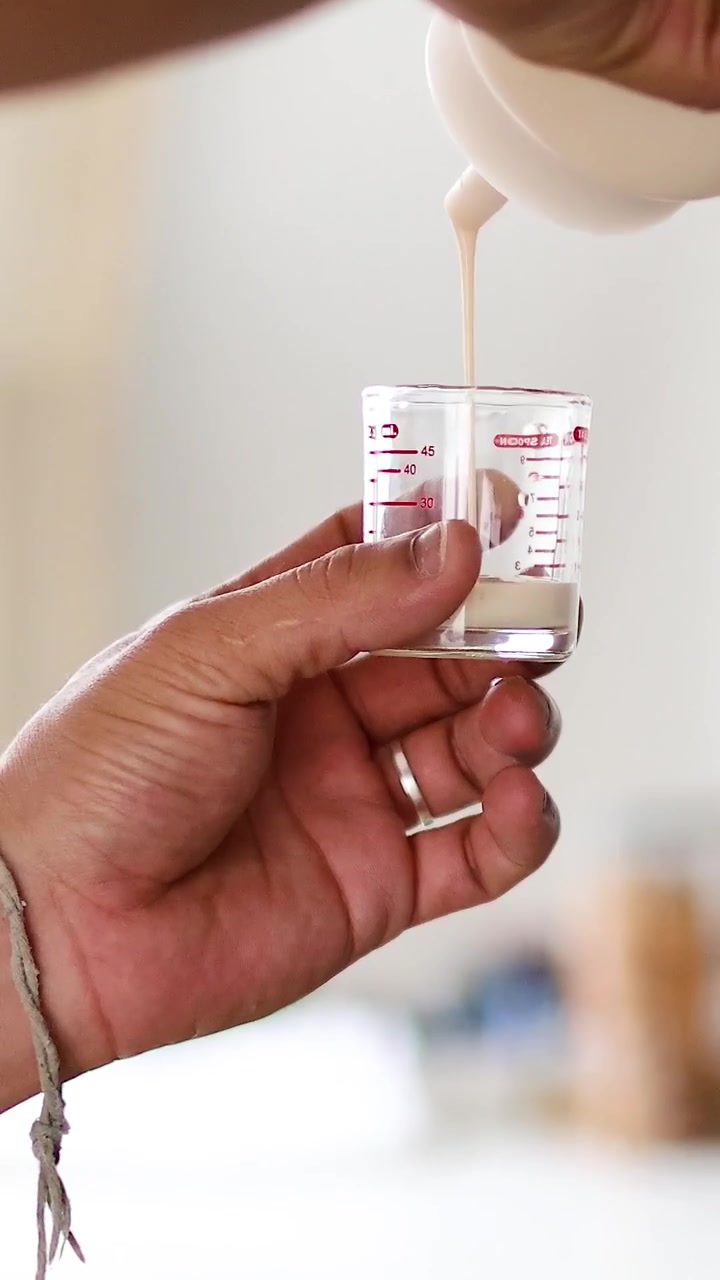 Eine Hand hält einen kleinen Glasmessbecher, während Sahne aus einer Flasche gegossen wird