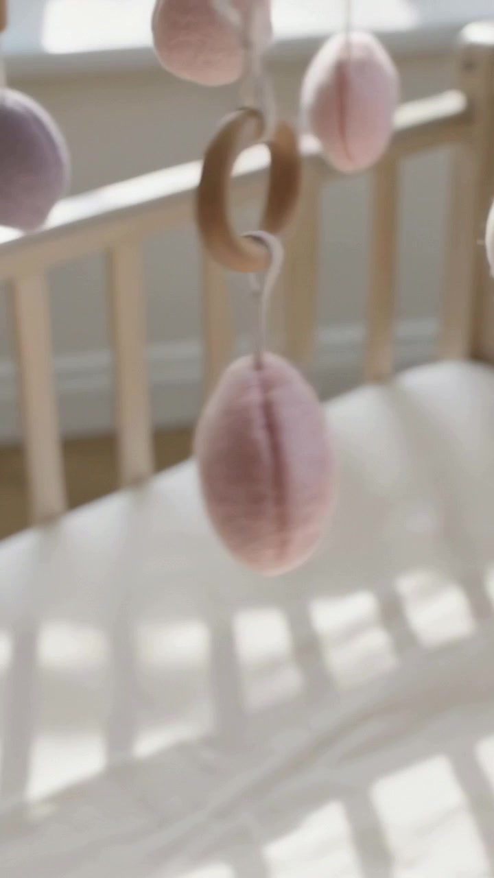 Vertical video: Shifting view and sunlight causing felt mobile turning above crib, wood ring