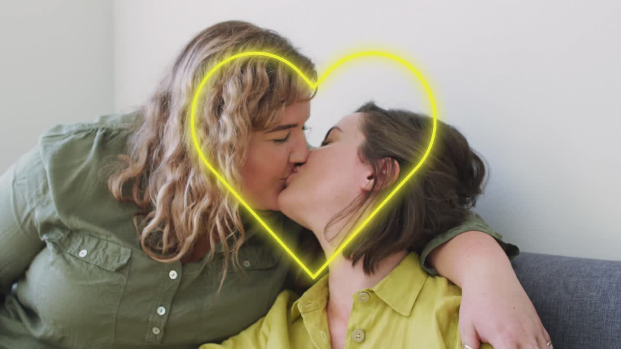 animación de corazón de neón sobre una feliz pareja de lesbianas caucásicas besándose en casa