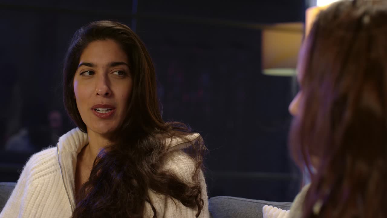 두 명의 여성 친구가 집이나 술집 또는 카페에서 소파에 앉아 함께 이야기하고 있습니다.