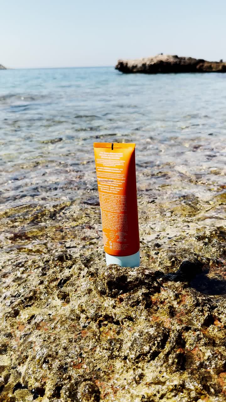 Sunscreen Bottle on Rocks by Clear Blue Sea at Beach
