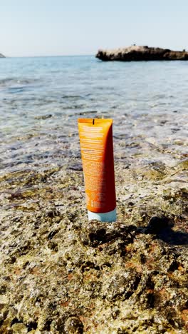 sunscreen bottle on rocks by clear blue sea at beach