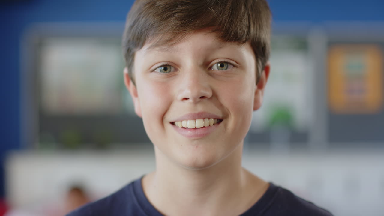 Smiling boy in school classroom looking at camera, feeling happy and confident