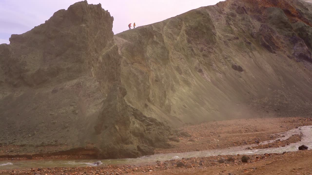 아이슬란드의 랜드만나라우가르에 있는 블라흐누쿠르 산을 등반하는 사람들의 실루, 앞면에는 강과 초록색 절벽이 있습니다.