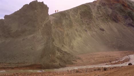 silhouette of people climbing bláhnúkur mountain in landmannalaugar, iceland, with a river and green cliff in the foreground