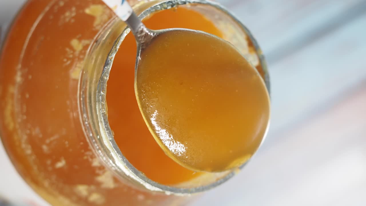 Un cucchiaio di miele dorato sollevato da un barattolo di vetro