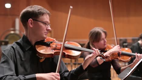 musicians in black clothes play violins rehearsing a performance