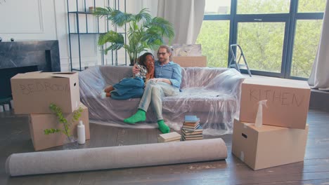 young cheerful couple man and woman hugging sits on sofa among relocation boxes