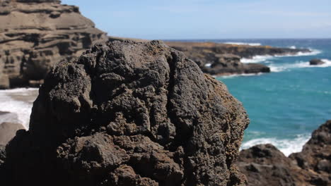 waves crash against shore behind black rocks on green sand beach in hawaii