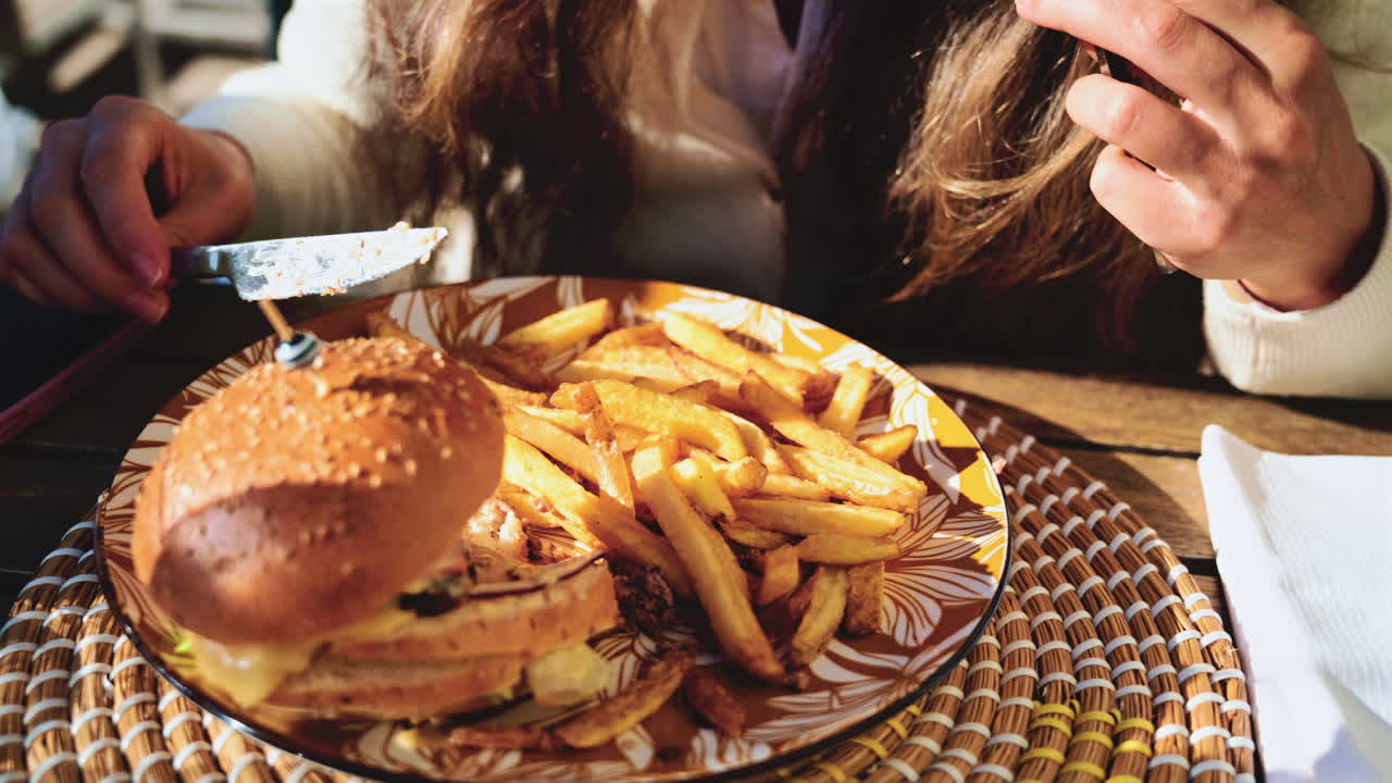 Gourmet burger served on a patterned plate in bright daylight, with blurred restaurant terrace in the background