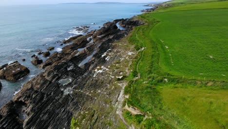 rugged coast drone footage flyover backwards with green fields, walk path and blue ocean