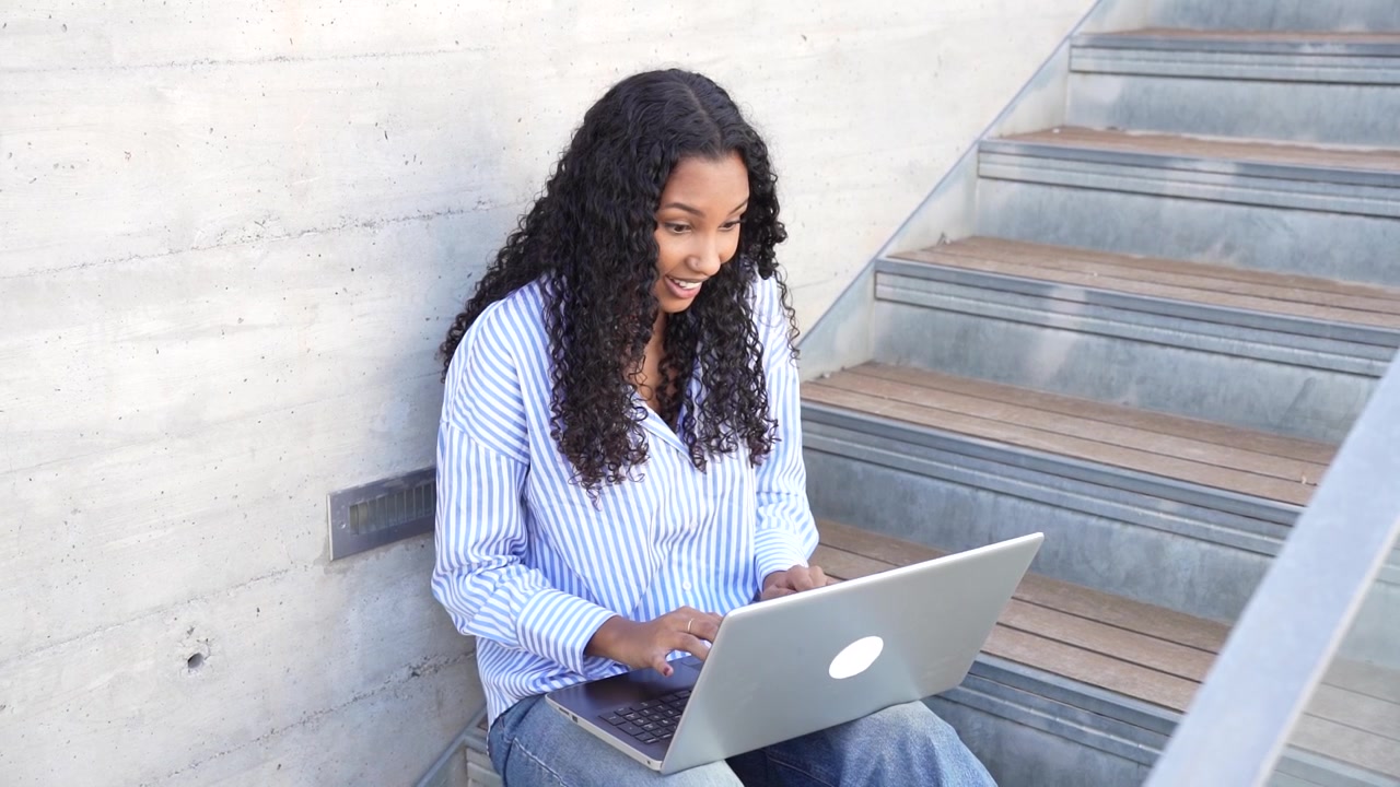 A young woman working on her laptop in a modern outdoor space surrounded by nature