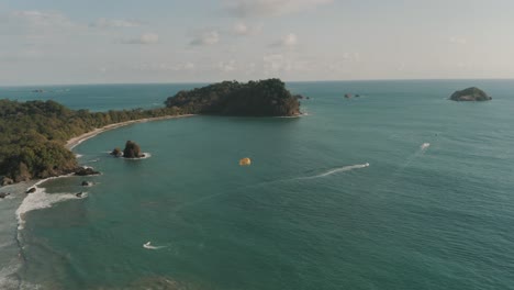 Schöne-Drohnenluftaufnahme-Von-Menschen,-Die-Im-Sommer-In-Costa-Rica-Am-Strand-Paragleiten