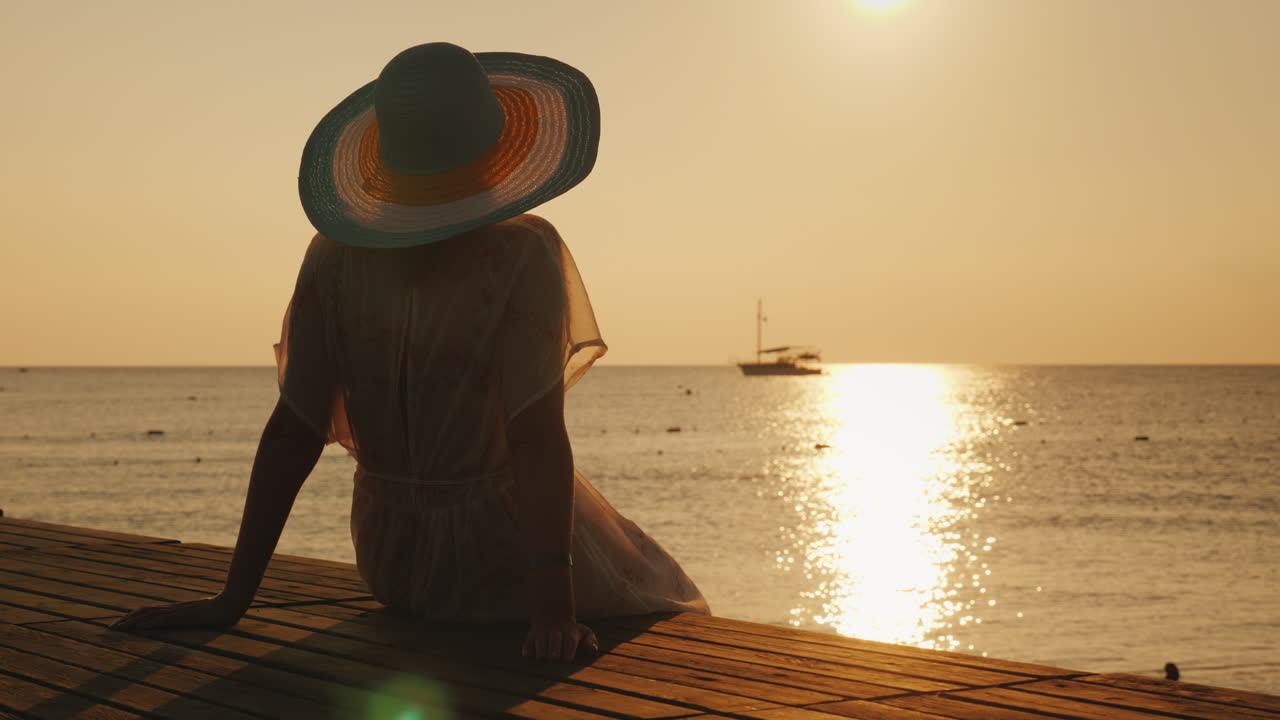 una joven se encuentra con el amanecer en el muelle, se sienta y mira el sol y el barco en el mar dre