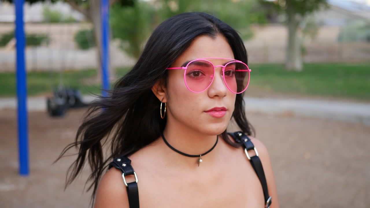 una joven hispana hipster con ropa de moda vintage y gafas de sol de aviador rosa retro en un parque infantil