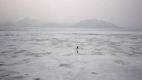 Dramatic-aerial-of-woman-walking-in-dress-in-Utah-desert-salt-flat