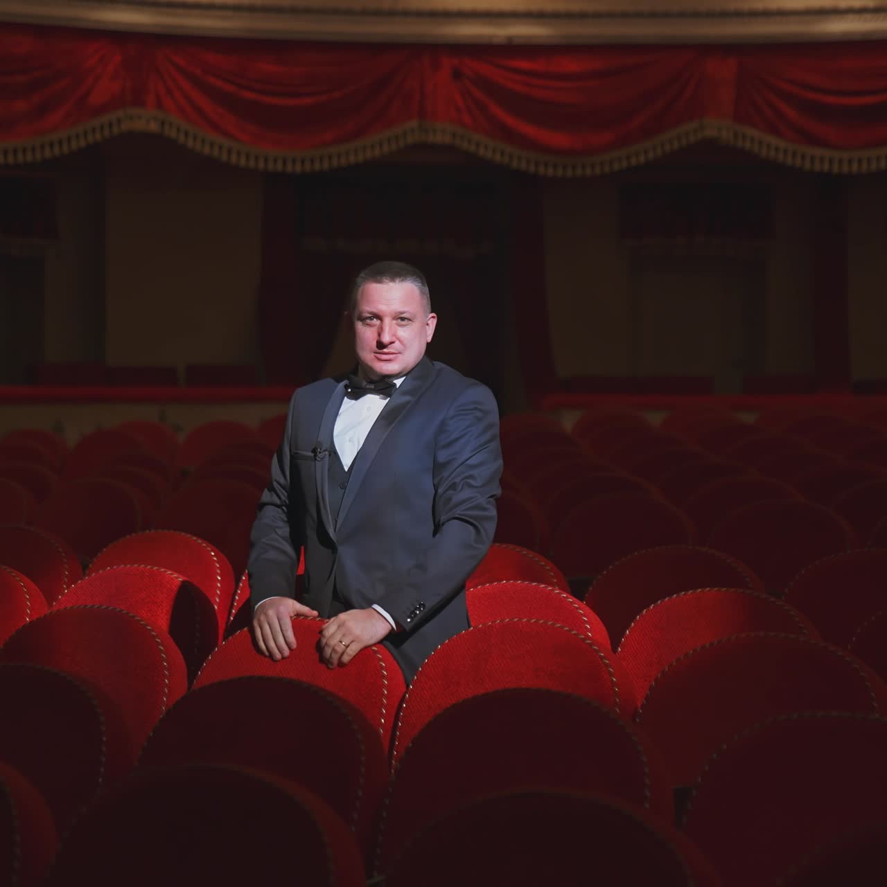 hombre feliz en la oscura sala de teatro vacía. hombre rico en traje de pie entre los sillones rojos vacantes en el gran auditorio y bailando alegremente solo.