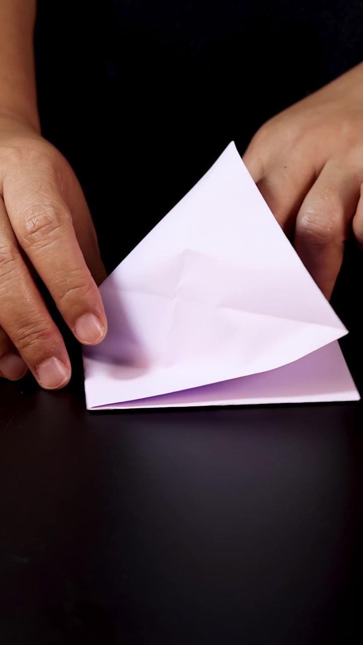 Manos doblando cuidadosamente papel blanco para origami, en primer plano, bajo iluminación suave y uniforme, con cámara estática.