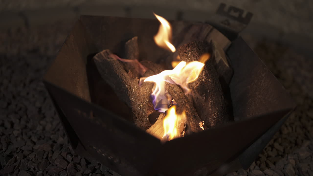 Bålflammer, der stiger op fra træstammer i et metalbålsted med intens varme og mørk natstemning, medium bane