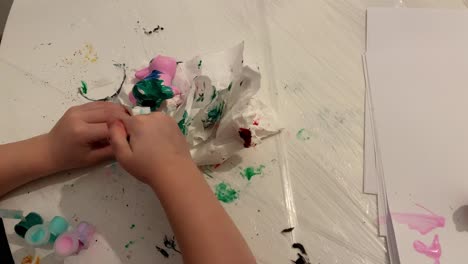 top view. child wipe hands in a white handkerchief. colourful paints on the table