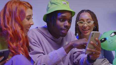 close up studio shot of young gen z friends sitting on sofa sharing social media post on mobile phones 6