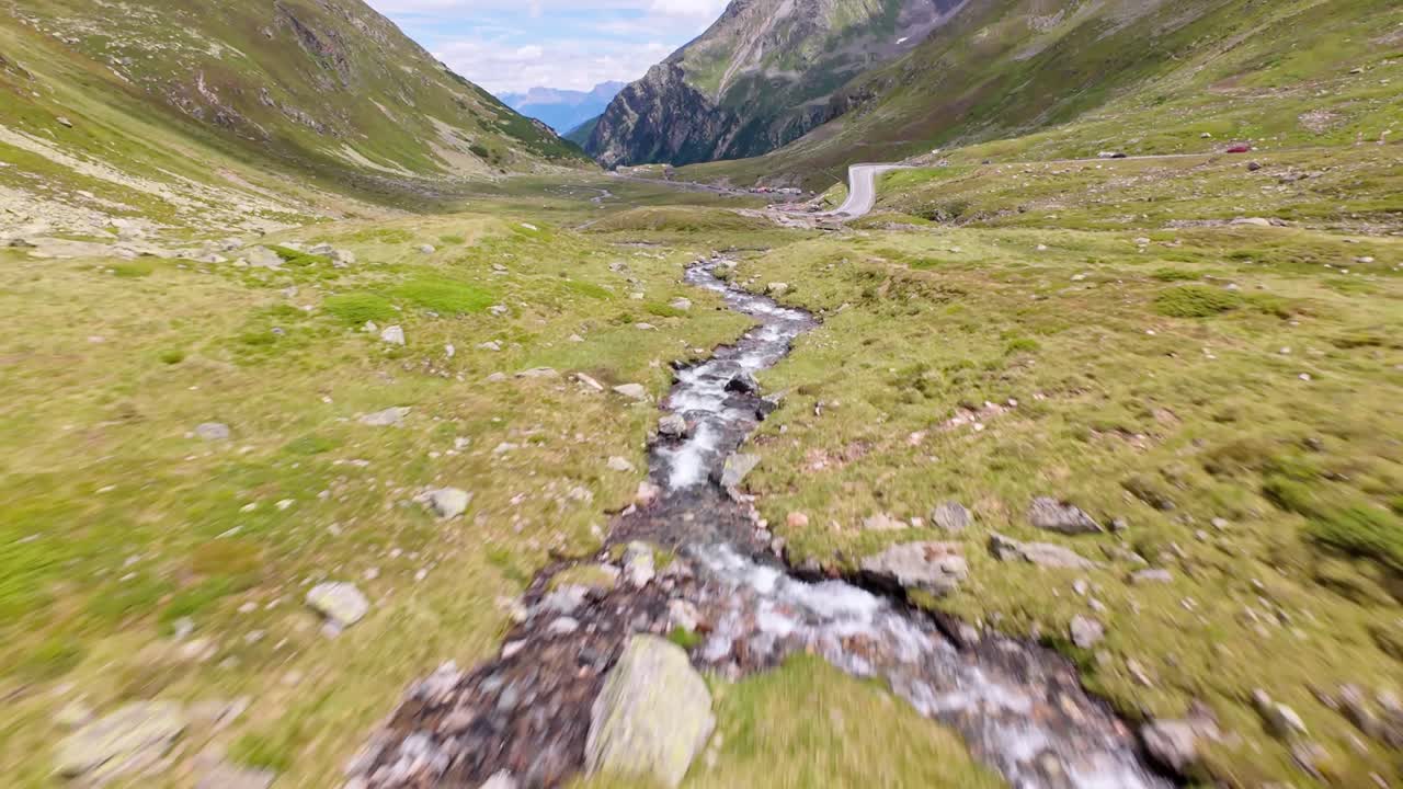 Stunning low aerial shot of a wide alpine valley with lush green grassland, framed by towering mountain peaks. A cinematic scene showcasing untouched nature and breathtaking wilderness