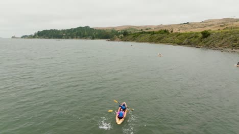 Toma-De-Adelantamiento-De-Personas-Navegando-En-Kayak-Hacia-La-Hermosa-Costa-De-Bahia-Tomales,-California