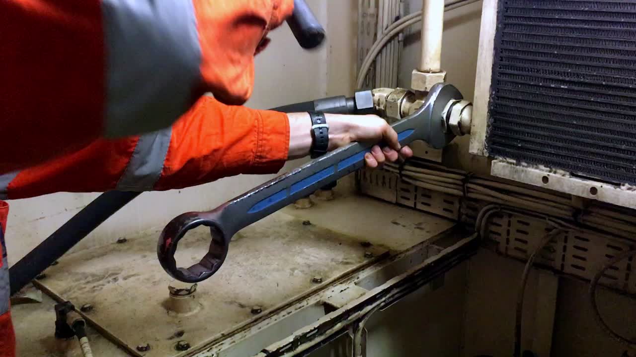 ingeniero en su uniforme industrial apretando un objeto usando una gran llave de metal y un martillo dentro del barco