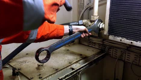 Engineer-in-his-industrial-uniform-tightening-an-object-using-big-metal-wrench-and-a-hammer-inside-ship