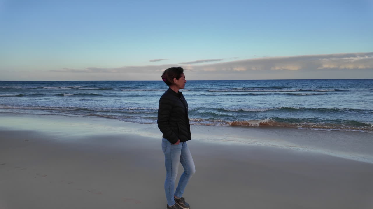 woman walking along the shoreline of a Fuerteventura beach during a calm evening