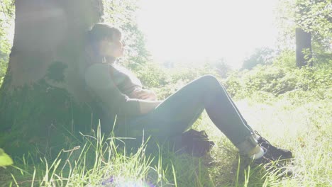 girl rests against trunk of tree in warm sunlight, lens flare